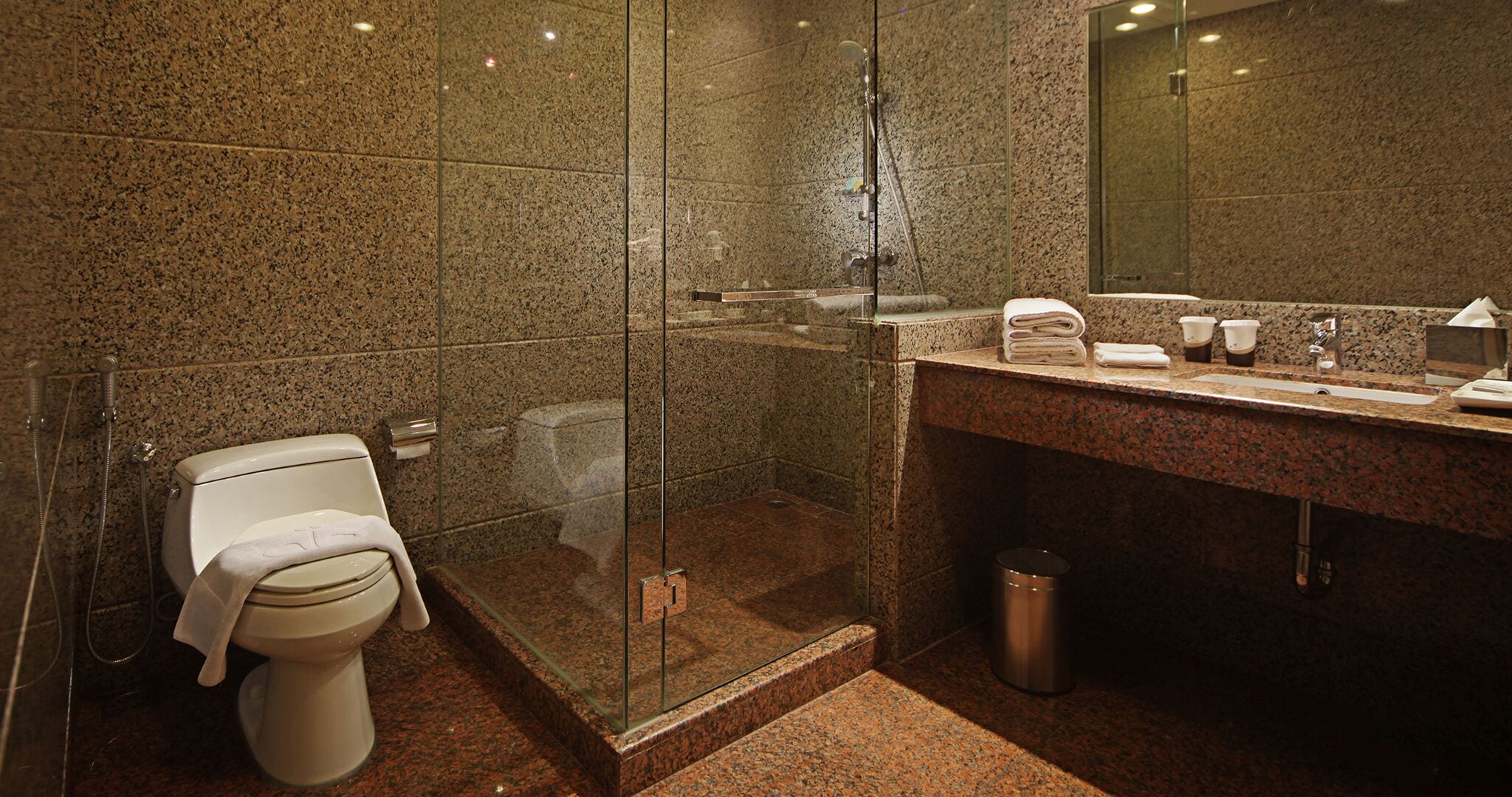 Un baño moderno con ducha de vidrio, inodoro, lavabo con espejo y cubo de basura.