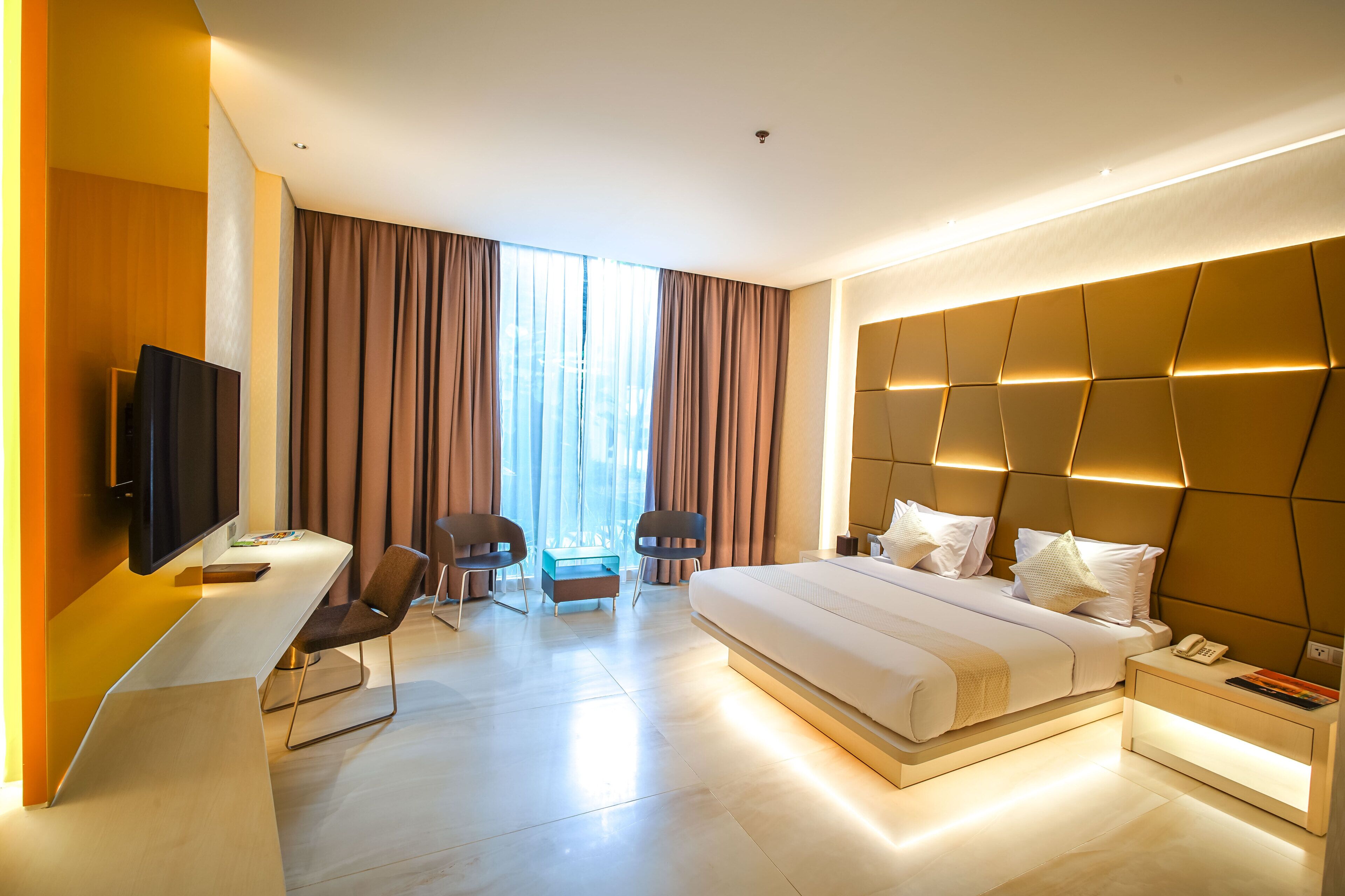 Habitación de hotel moderna con una cama grande, un escritorio con televisor de pantalla plana, dos sillas, una mesita pequeña y una mesita de noche con teléfono.