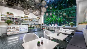 Un caffè moderno con arredi bianchi, diverse piante e un'ampia vetrata vista verde.