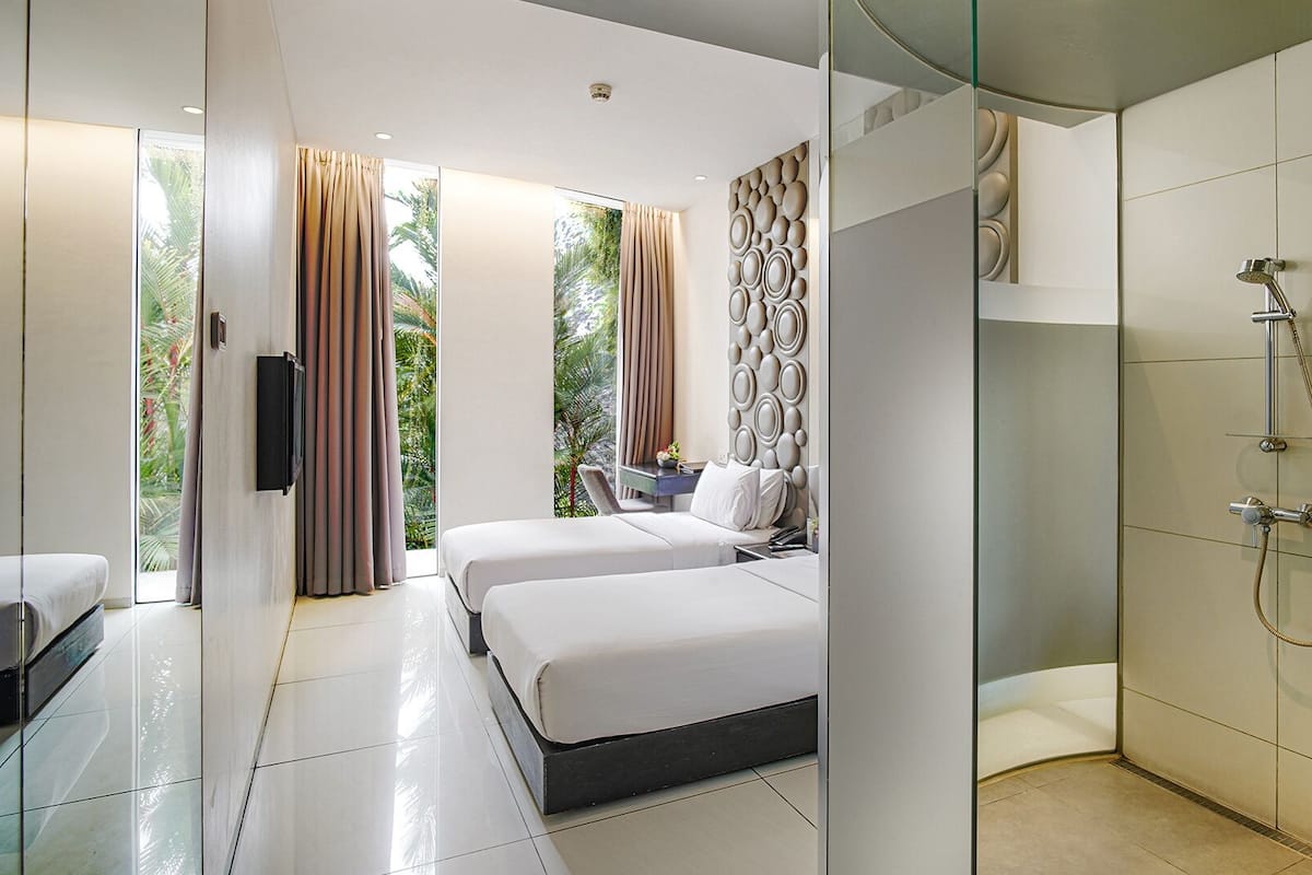 A modern bedroom with a glass shower enclosure, a bed with white linens, and a view of greenery outside.