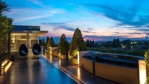 Una terrazza panoramica moderna con zone relax, una piscina e vista sullo skyline della città al crepuscolo.