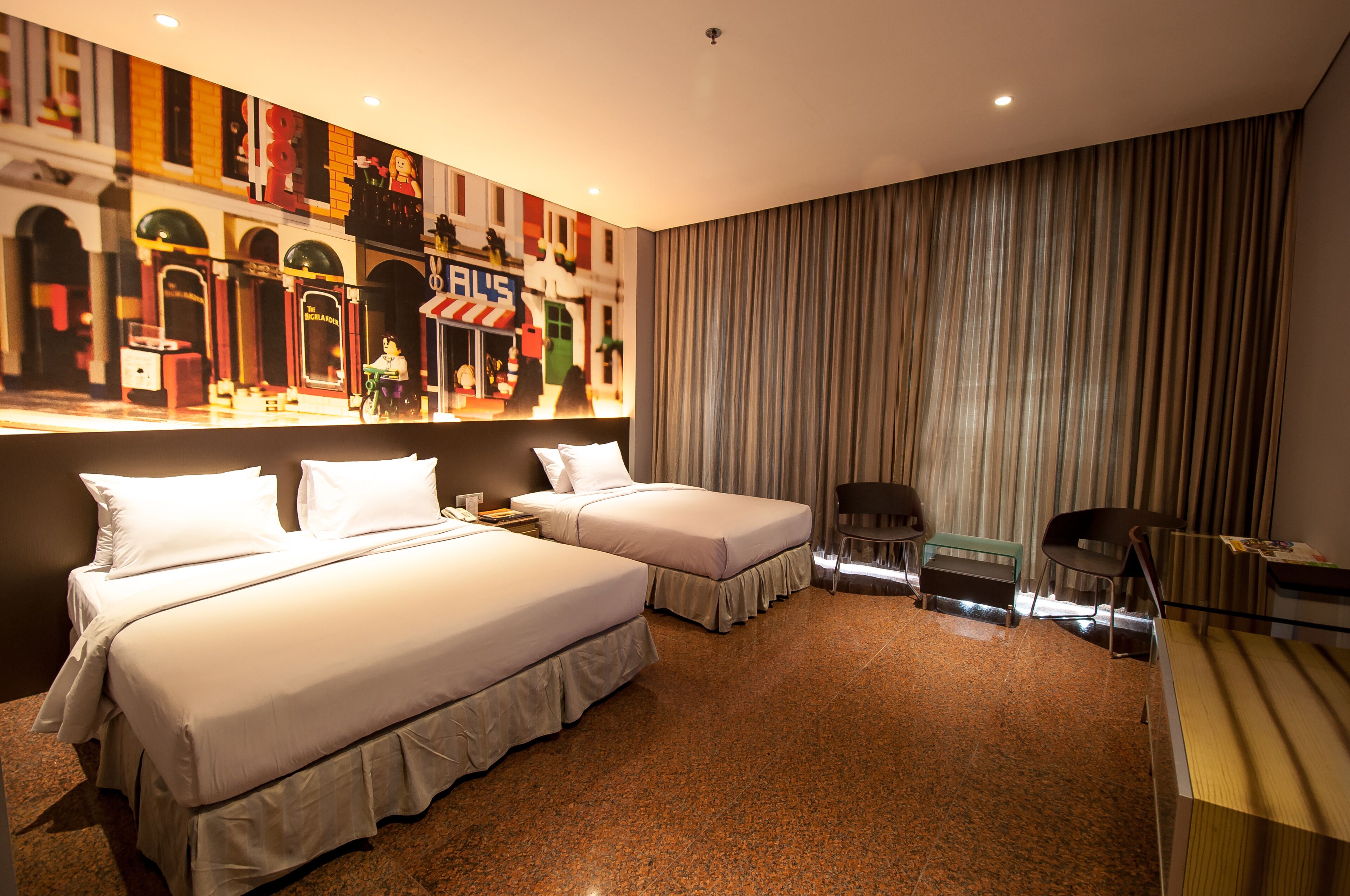 Habitación de hotel con dos camas, un escritorio, una silla, un ventanal con cortinas y un mural en la pared.