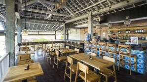 A restaurant with wooden tables and chairs, a bar area with blue and white tiles, and hanging pendant lights. - Adi Cottage (Ubud)