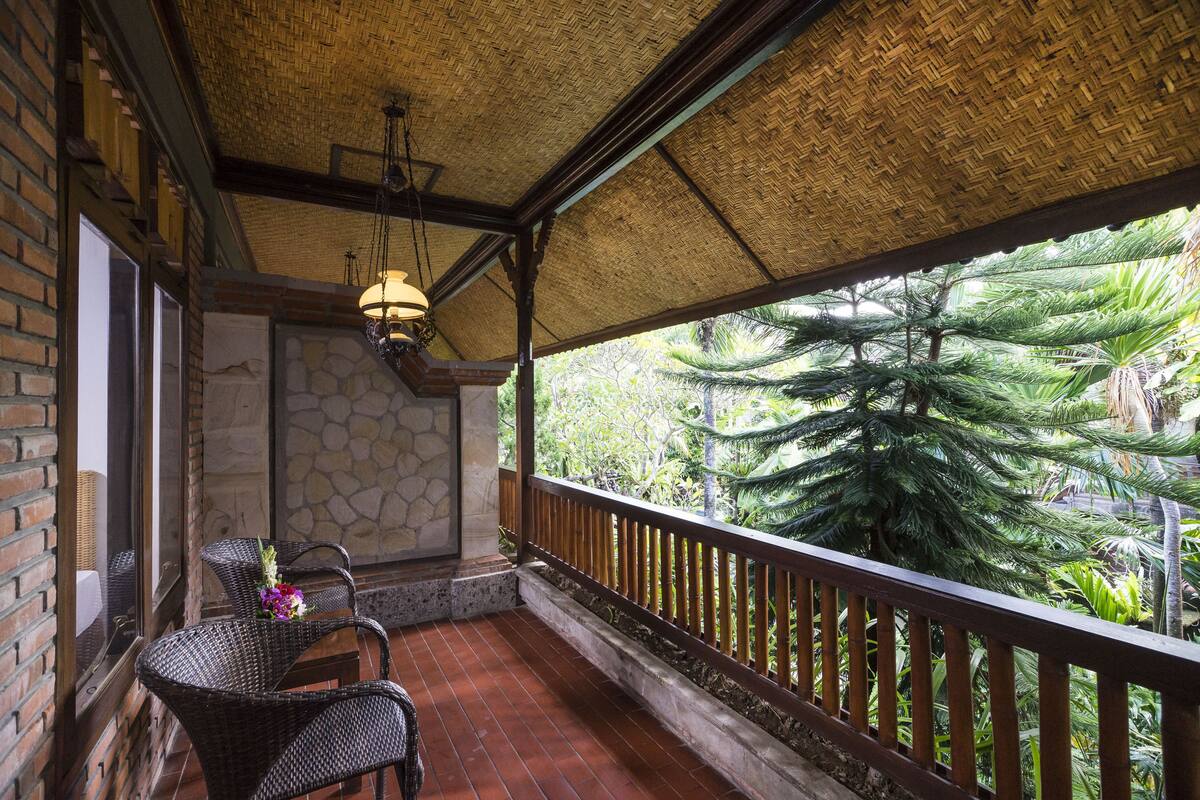 A covered balcony with wicker furniture, a stone wall, and a view of tropical vegetation.