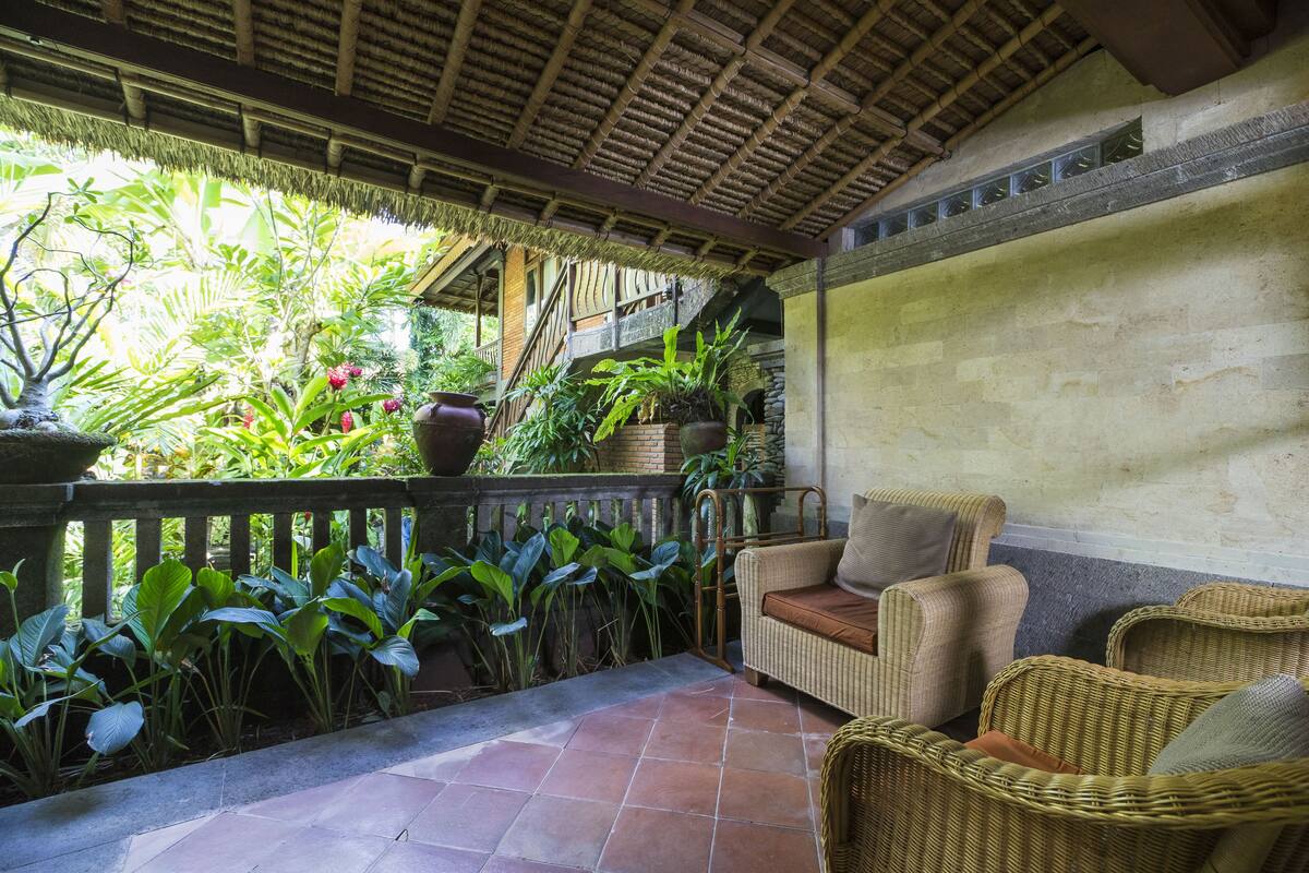 A covered patio with wicker furniture, potted plants, and a stone floor.