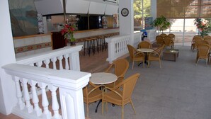 A bar area with stools, a counter, and a potted plant. There are wicker chairs and tables arranged for seating.