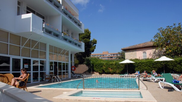 A pool area with lounge chairs and a building with balconies.