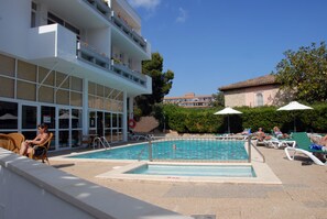 A pool area with lounge chairs and a building with balconies. - Apartamentos Marthas (Calvia)