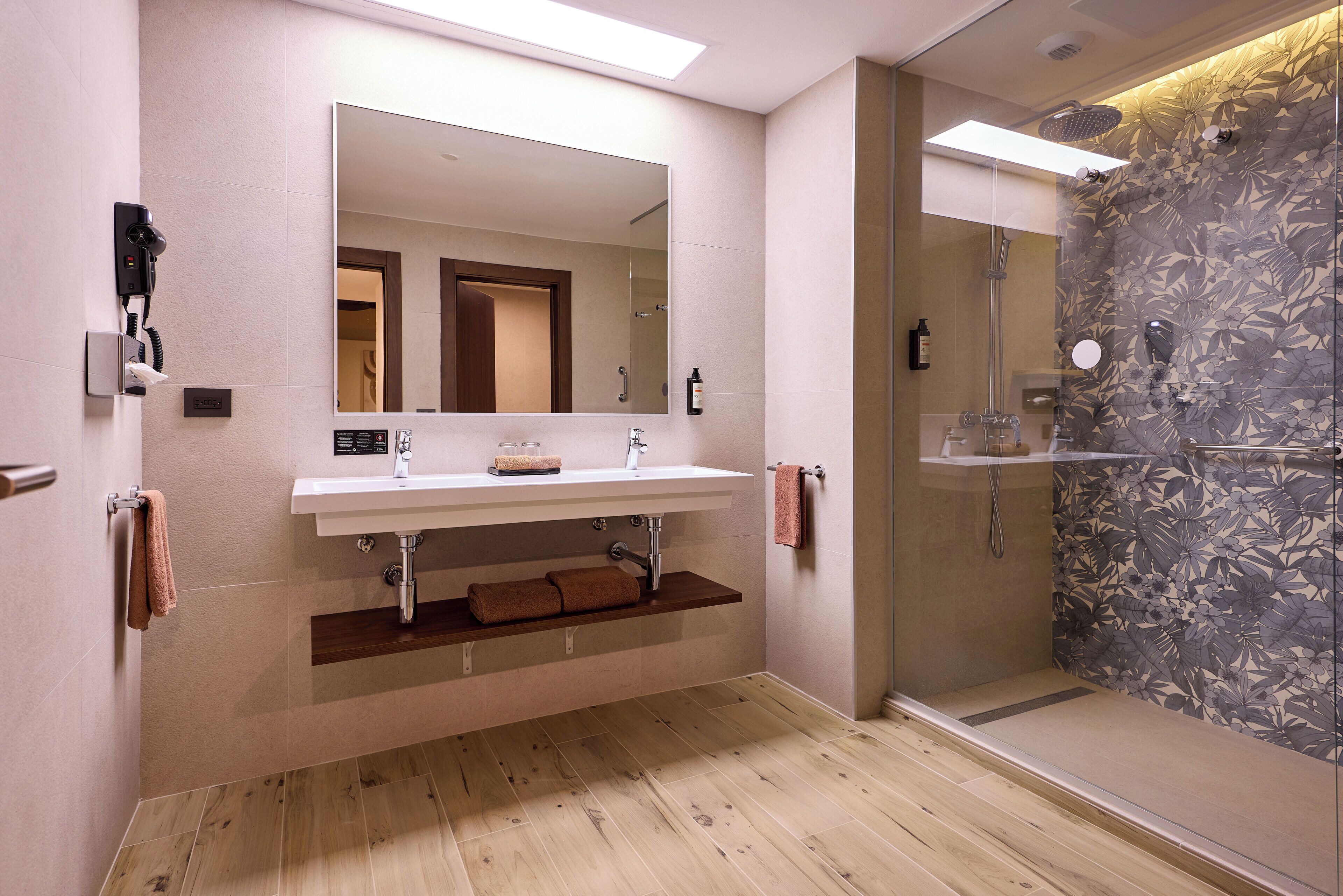 Un baño moderno con un espejo grande, un lavabo, una ducha y suelo de madera.