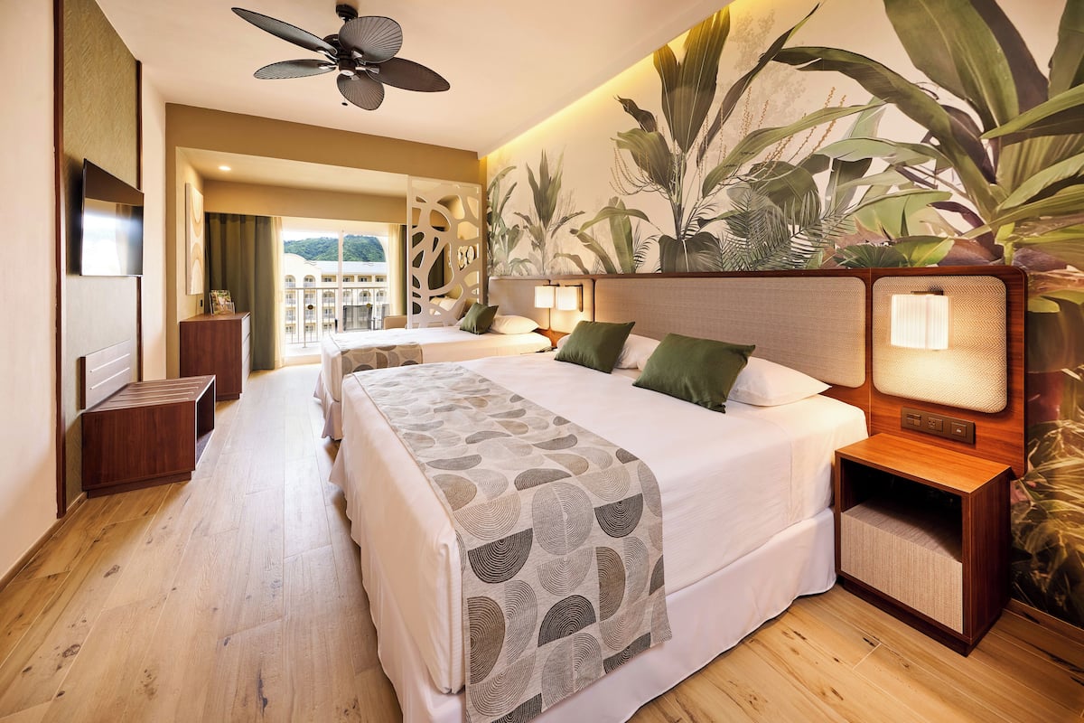 A hotel room with a large bed, bedside tables, a ceiling fan, and a view of the outside.
