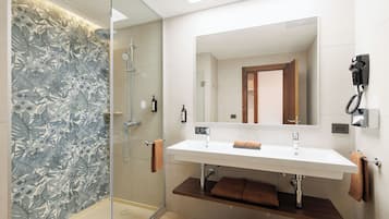 Une salle de bain moderne avec une douche à parois de verre, un grand miroir et un lavabo double avec une étagère en bois en dessous.
