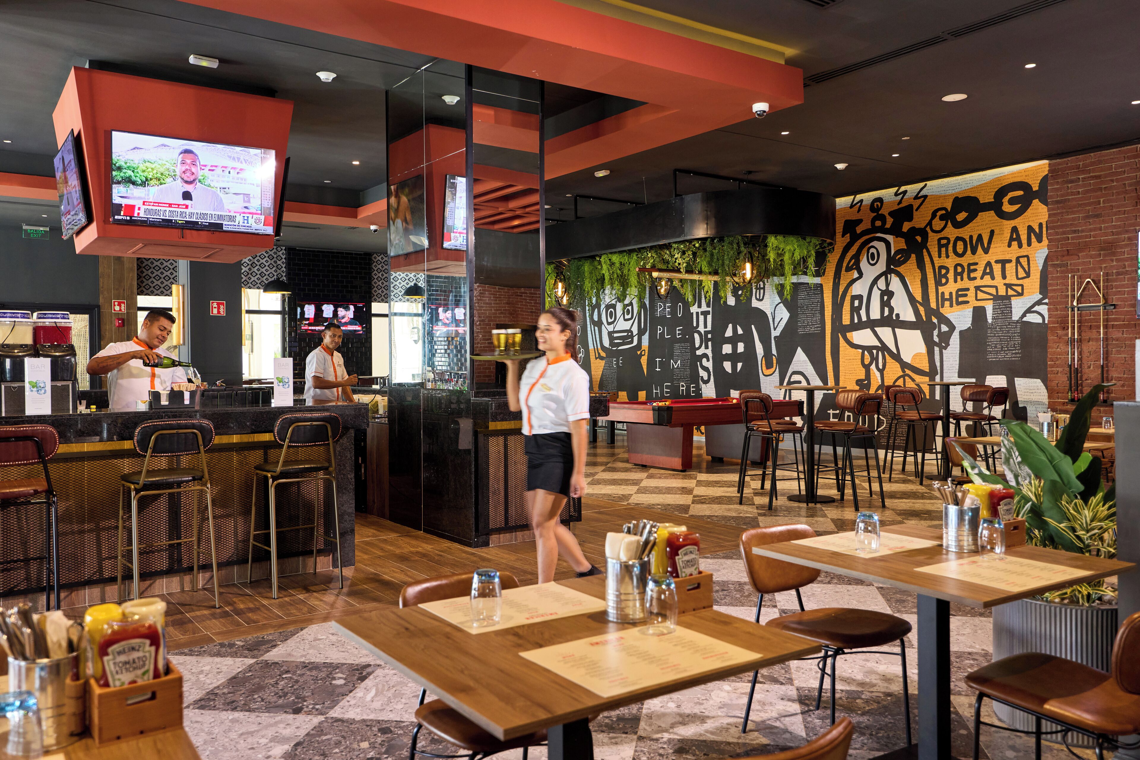 A restaurant with a bar area, tables with menus, and a mural on the wall.