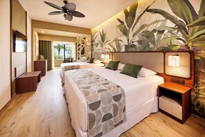 A hotel room with a large bed, two bedside tables, a ceiling fan, and a wall mural of tropical plants.