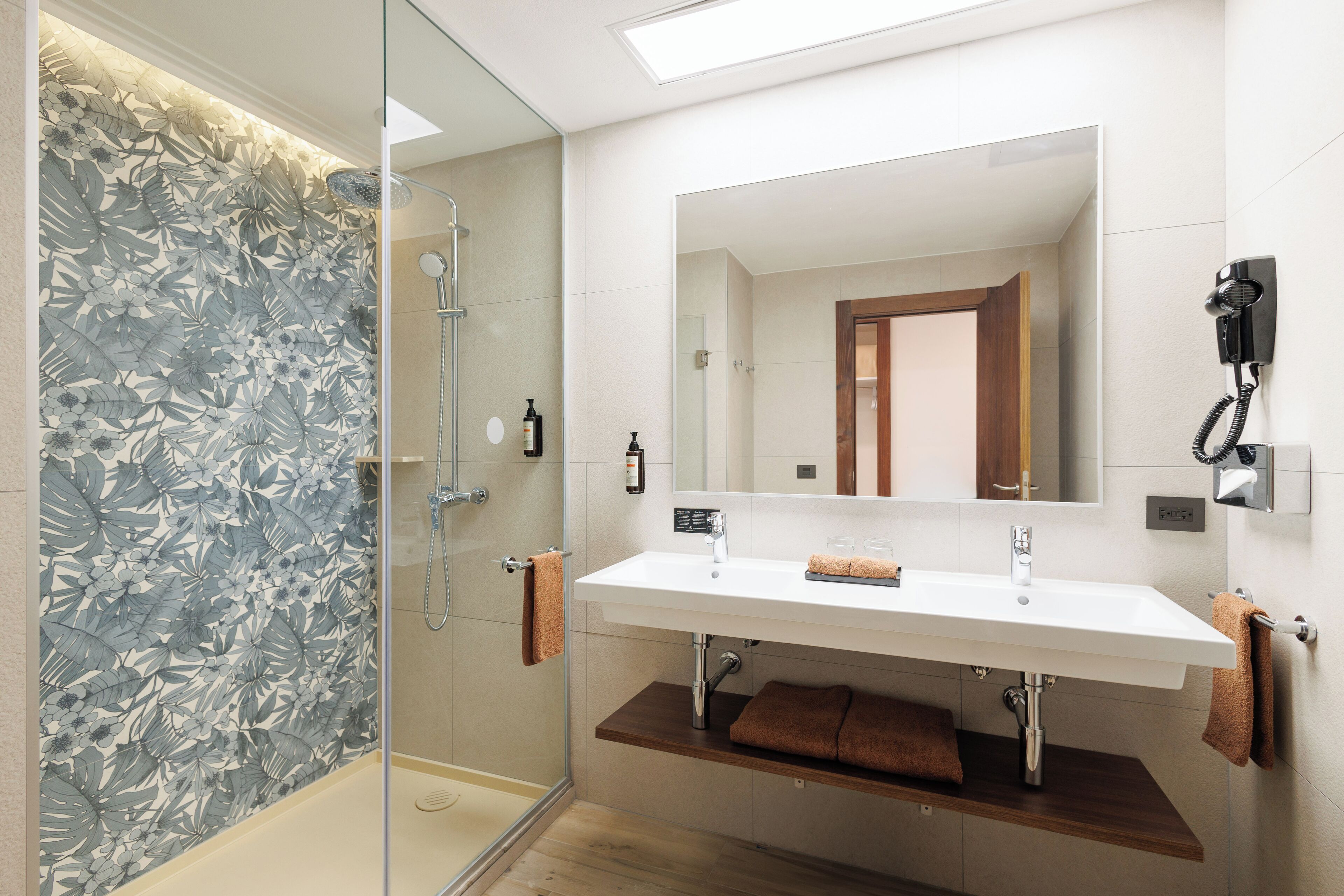 A modern bathroom with a glass shower enclosure, a double sink vanity, and a large mirror.