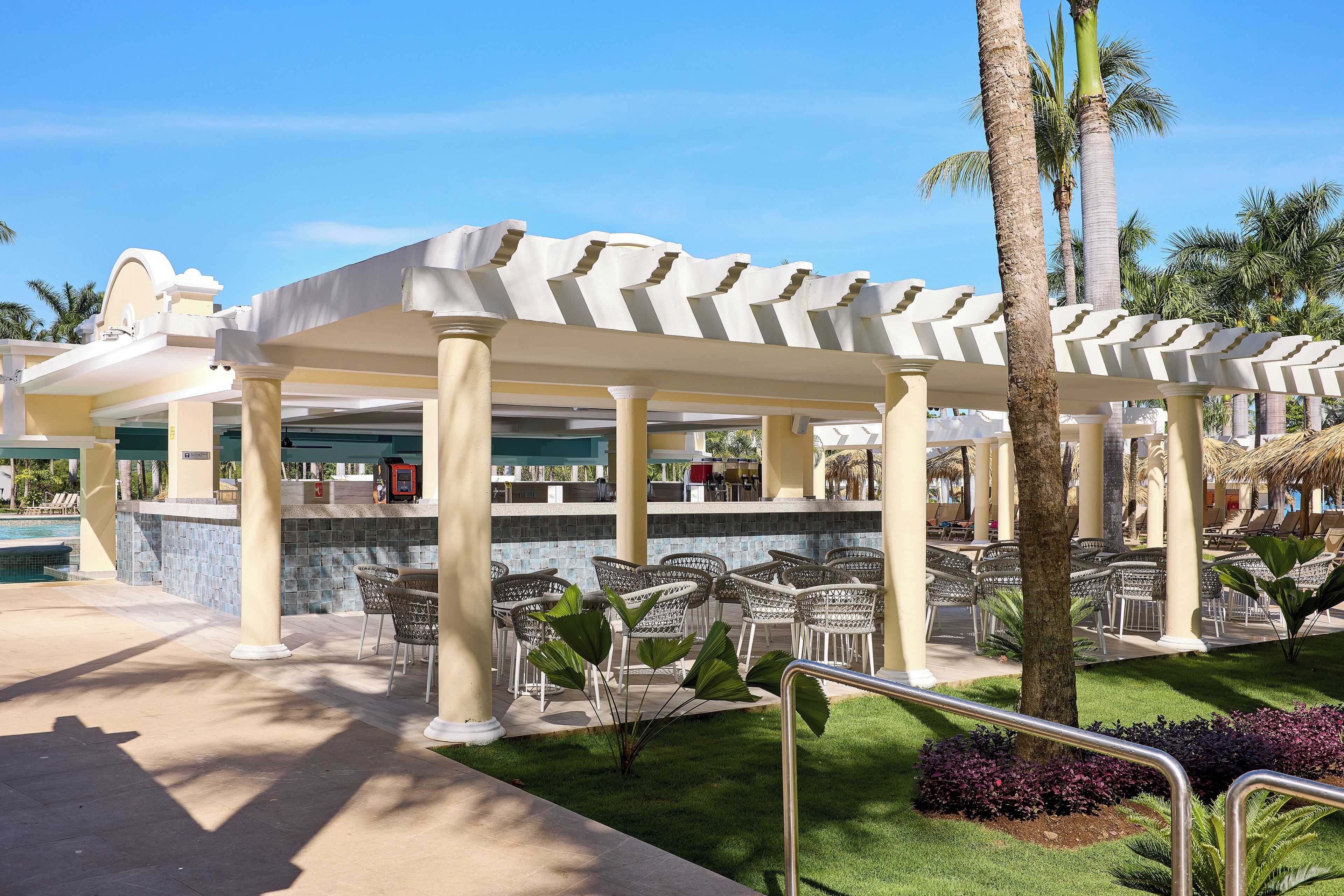 A covered outdoor seating area with chairs and a pool in the background.