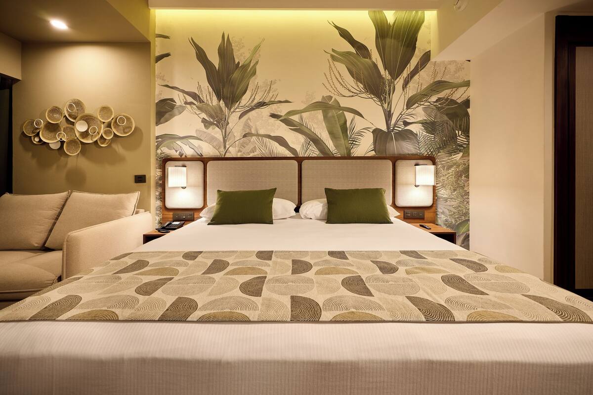 A hotel room with a large bed, two bedside lamps, a wall-mounted clock, and a decorative wall panel.