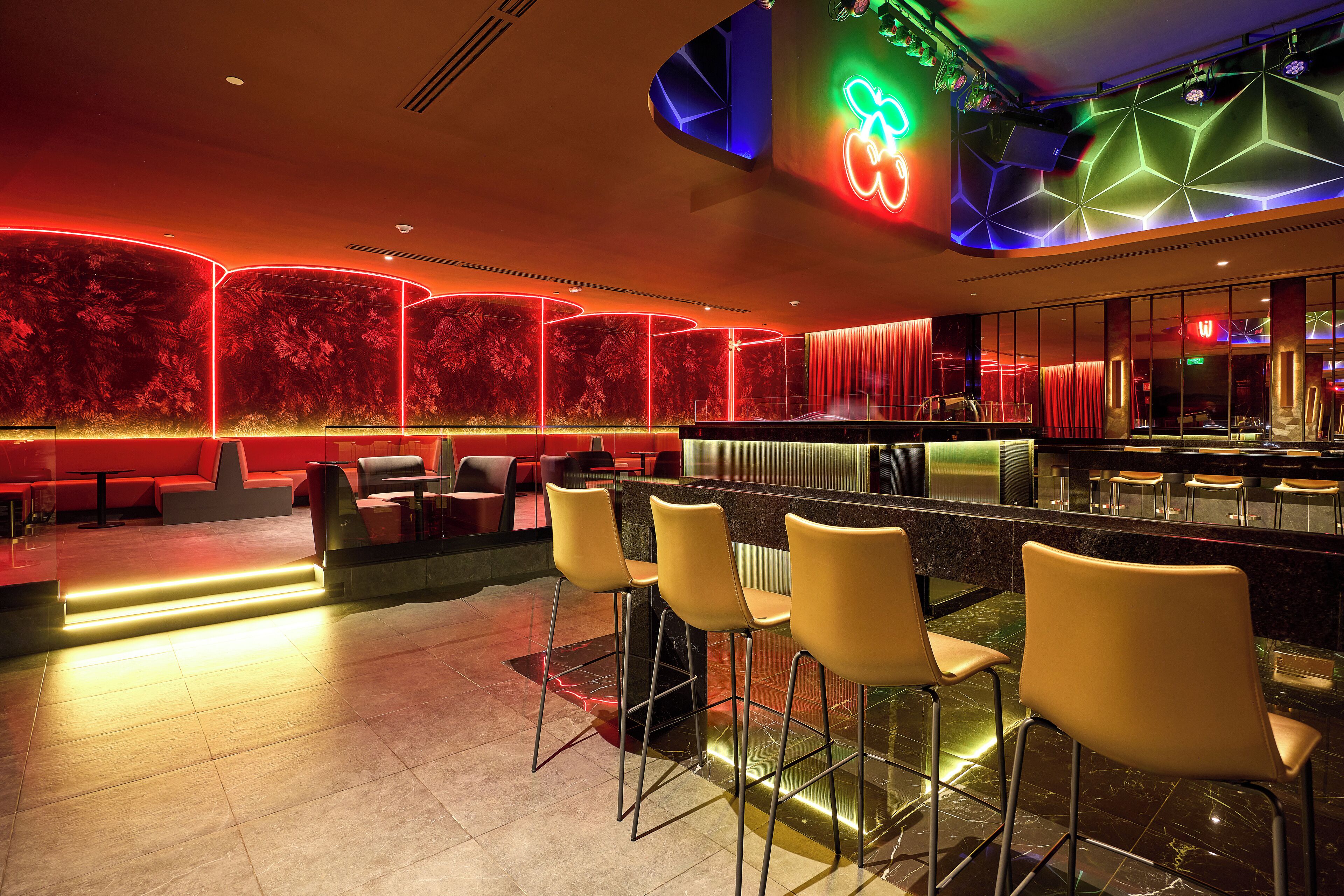 Un espacio moderno de bar con iluminación de neón, una barra y taburetes.