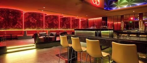 Un espacio moderno de bar con iluminación de neón, una barra y taburetes.