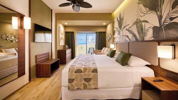 A hotel room with a large bed, a ceiling fan, a TV, and a balcony with a view.