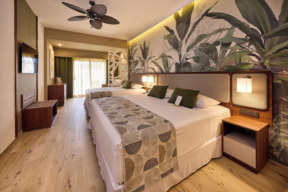 A hotel room with a bed, bedside tables, a ceiling fan, and a large plant wall.