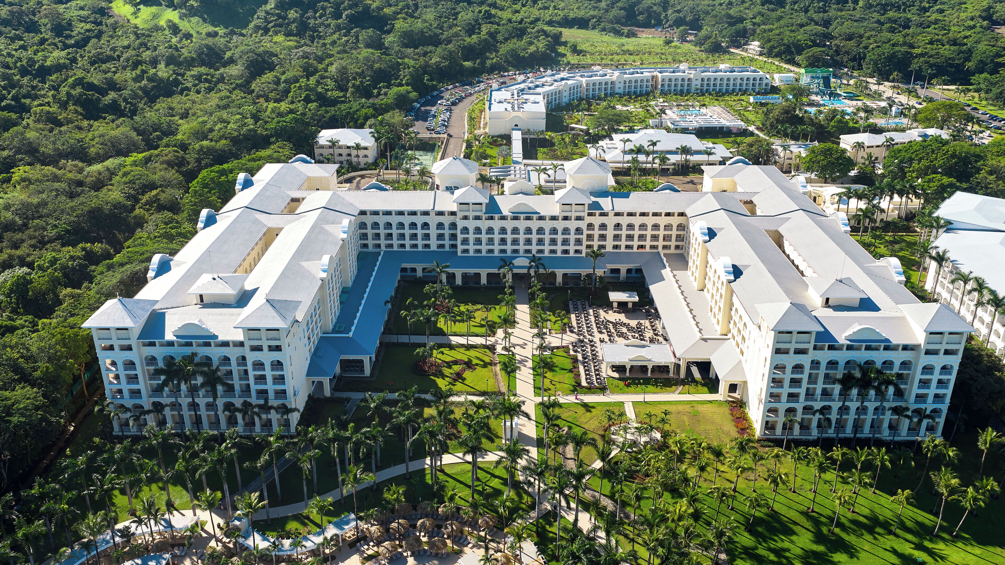 A large resort with multiple buildings, a central courtyard, and a pool area surrounded by palm trees.