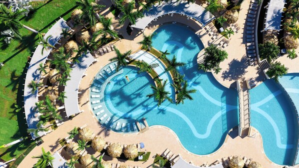 Vue aérienne d’un complexe hôtelier doté de plusieurs piscines, de palmiers et de chaises longues.