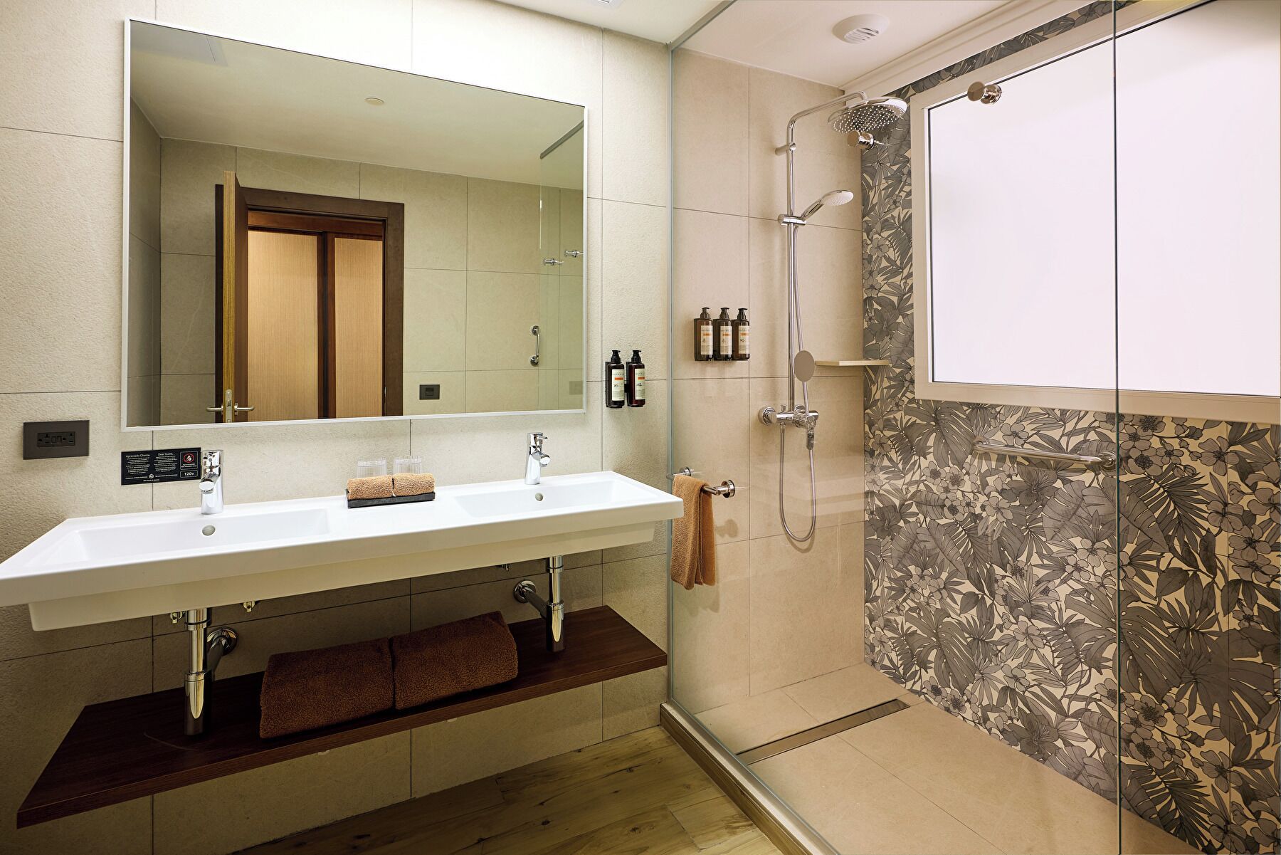 Un baño con lavamanos doble, espejo, ducha y pared con estampado floral.
