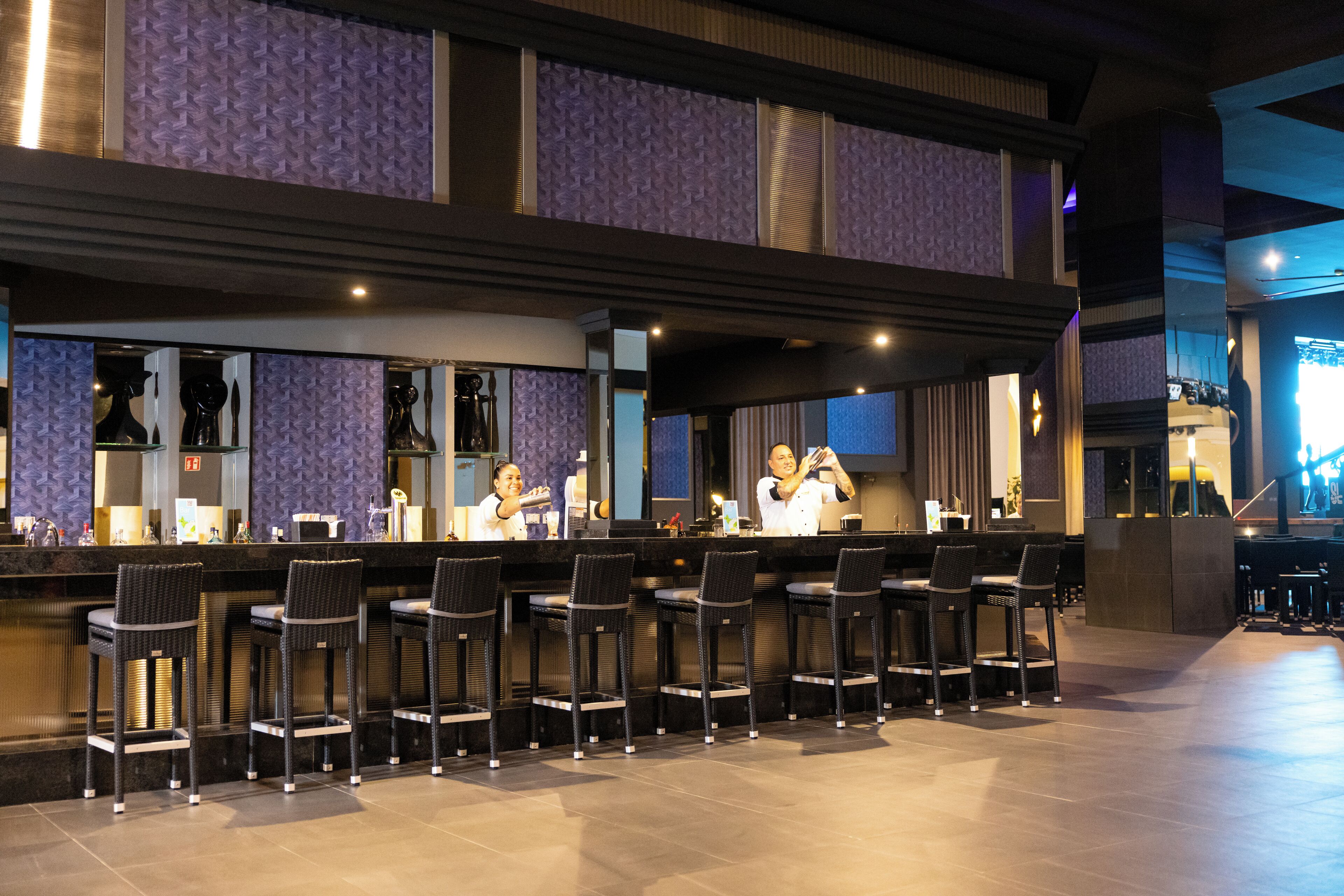 A bar area with a counter, bar stools, and a reflective wall.