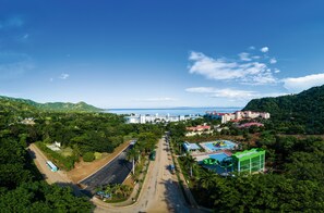 A resort with a swimming pool, a large building, and a road leading to the beach.