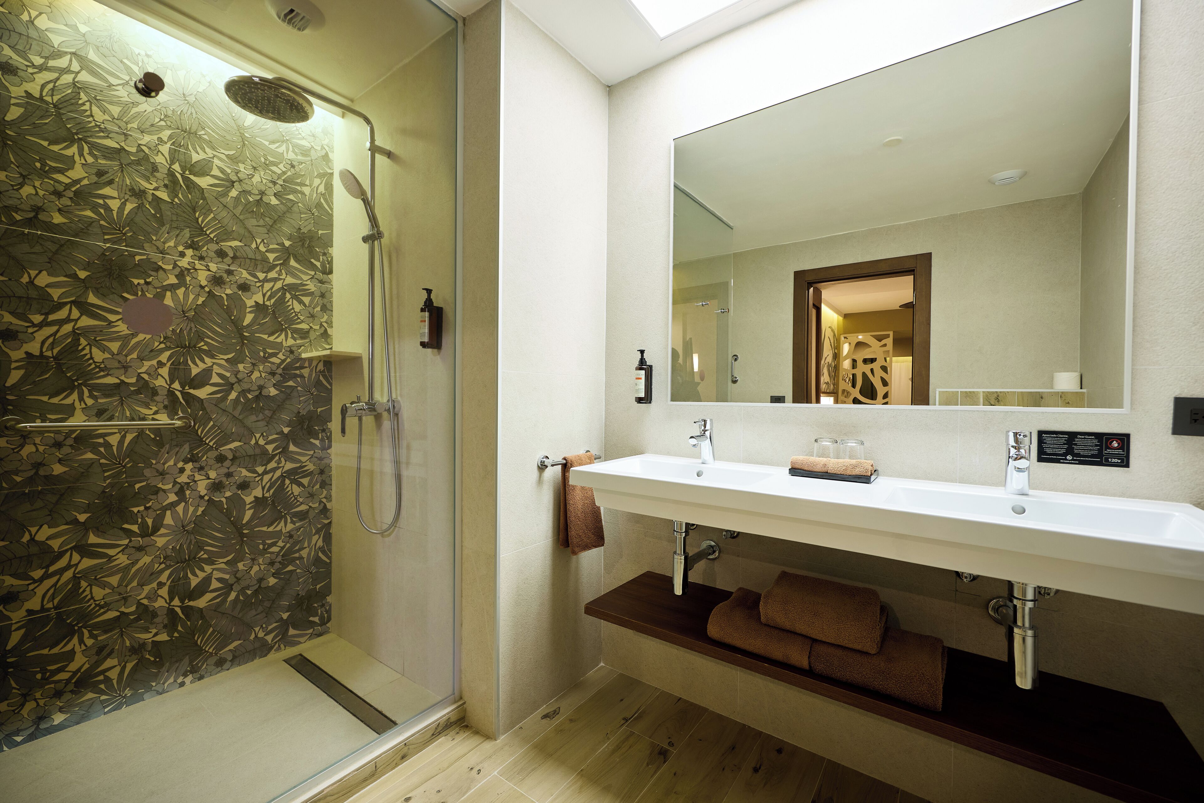 Un baño moderno con cabina de ducha de vidrio, un lavabo blanco con espejo encima y un estante de madera debajo.