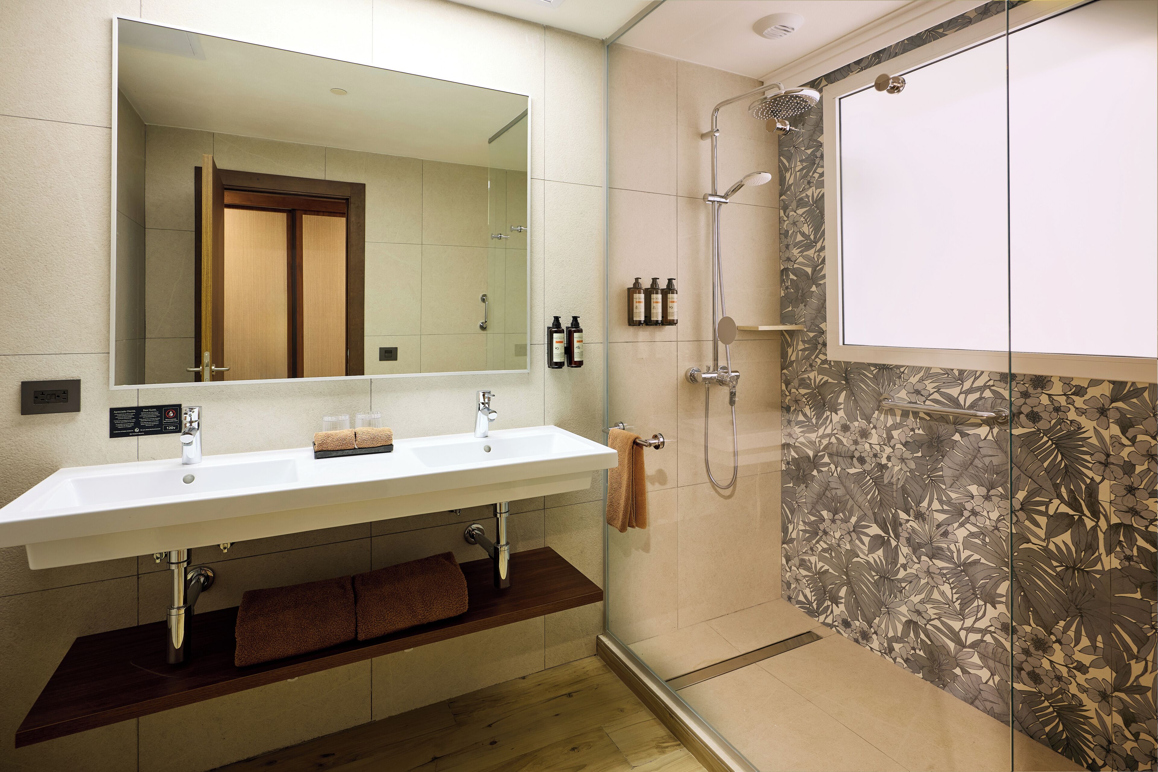 Un baño moderno con un espejo grande, dos lavamanos, una ducha y un mueble de tocador de madera.