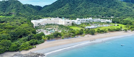 A resort with multiple buildings, a beach, and a mountainous backdrop.