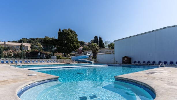A swimming pool with clear blue water, surrounded by lounge chairs and a small slide. - Vacanceole Residence L'Ile d'Or (La Londe-les-Maures)