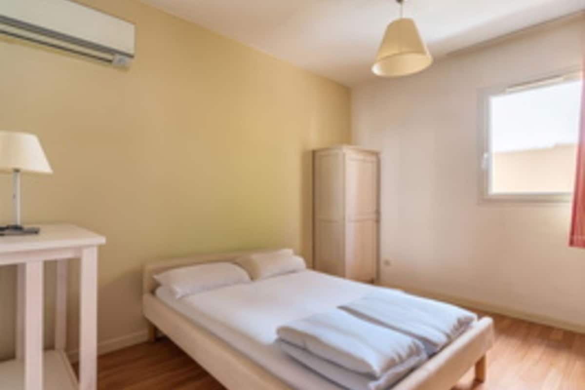 Ein Schlafzimmer mit Bett, Nachttisch, Lampe, Kleiderschrank und Fenster.