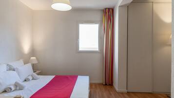 A hotel room with a bed, a window, a wardrobe, and a bedside table with a lamp.