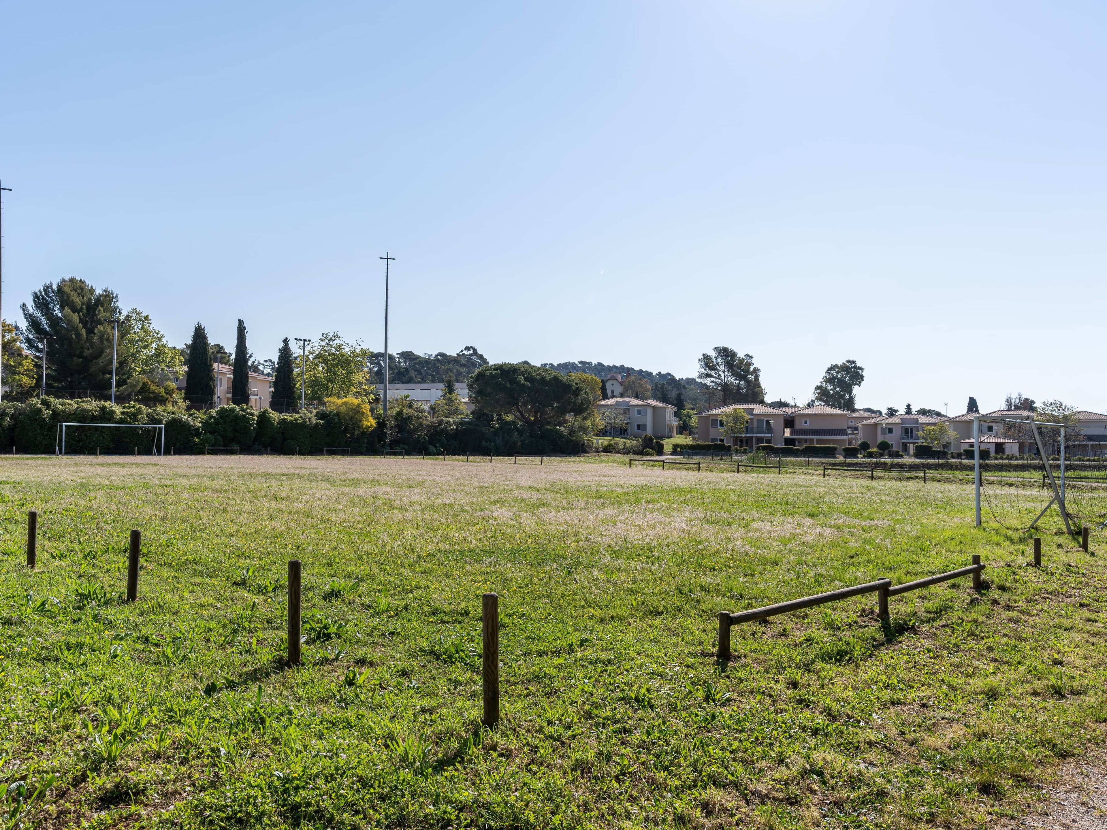 A grassy field with a soccer goal, surrounded by a fence and trees.