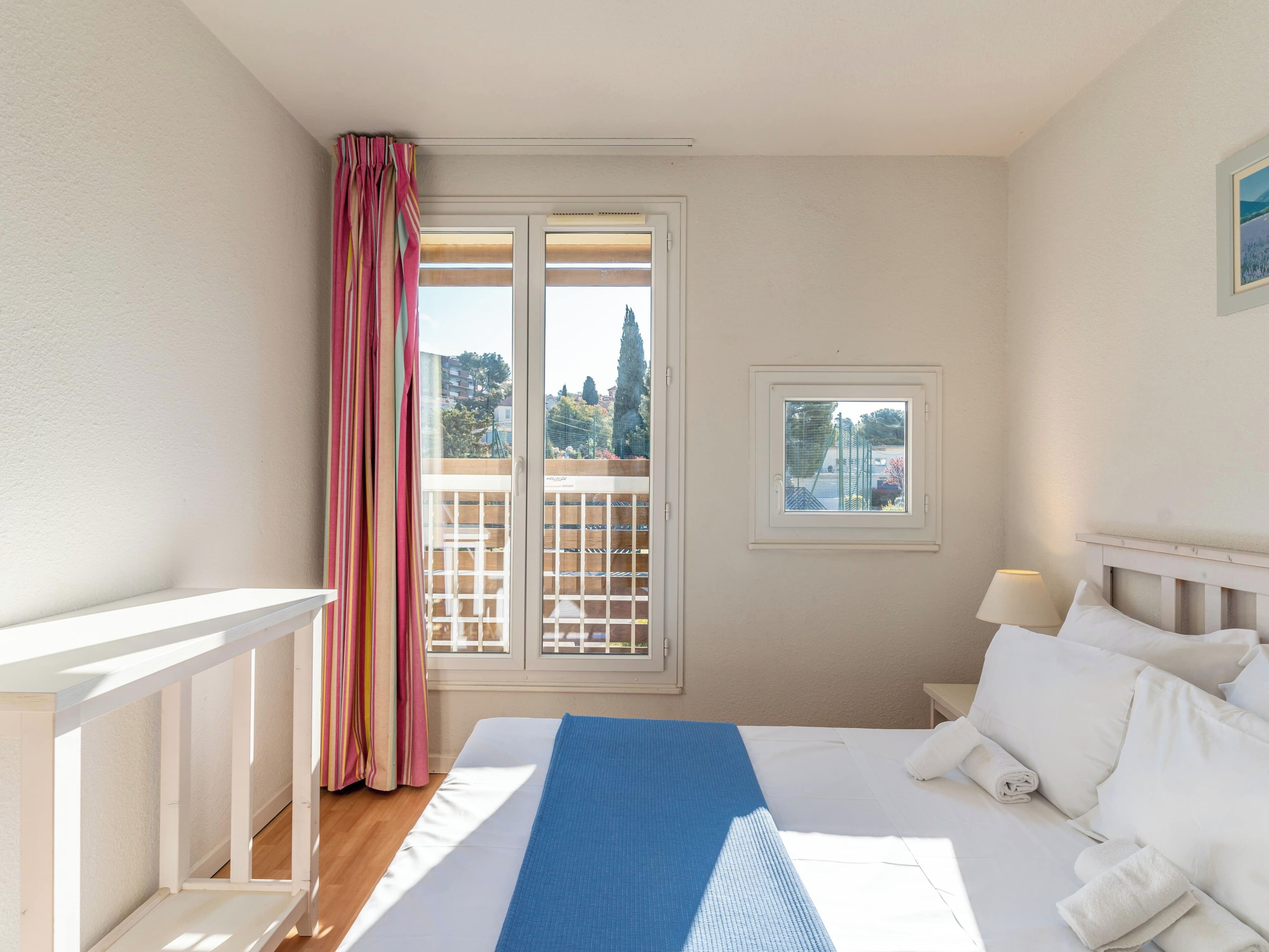Une chambre d’hôtel avec un lit, une fenêtre donnant sur un paysage agréable, une petite fenêtre et un rideau.