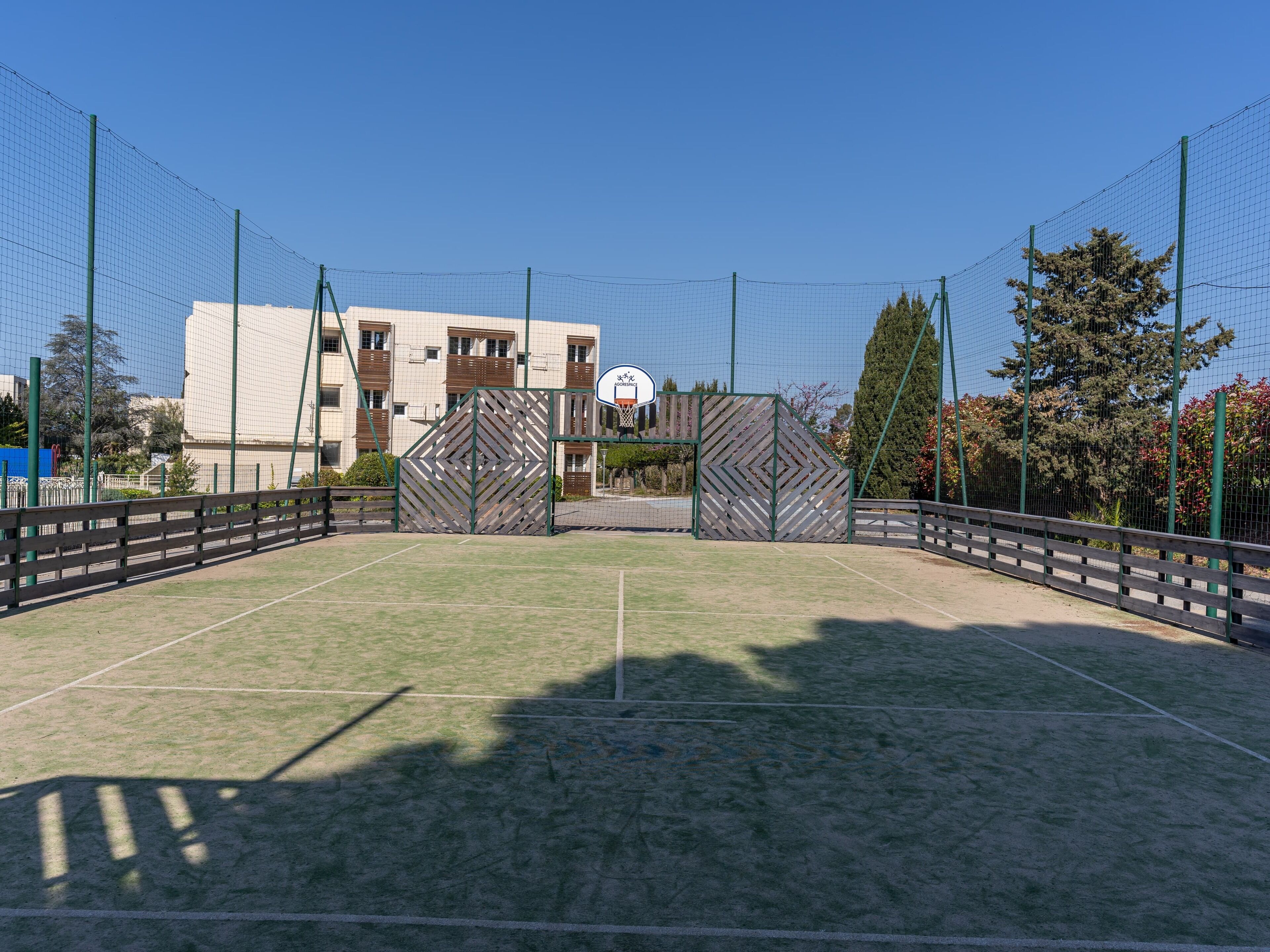 Una cancha de baloncesto al aire libre con aro, rodeada de una cerca y árboles.