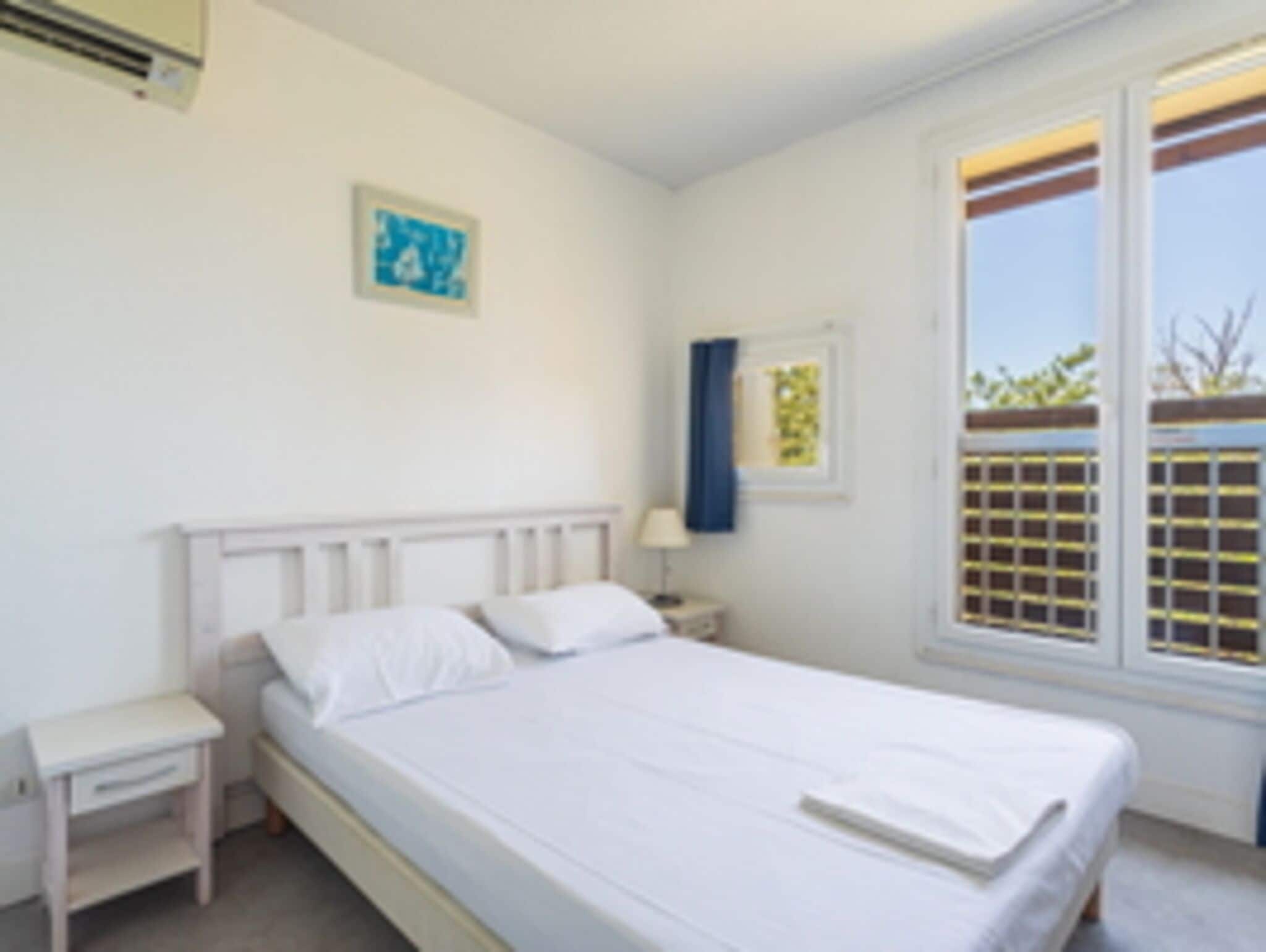 Une chambre avec un lit simple, une table de chevet, un climatiseur fixé au mur et une fenêtre donnant sur un paysage verdoyant.