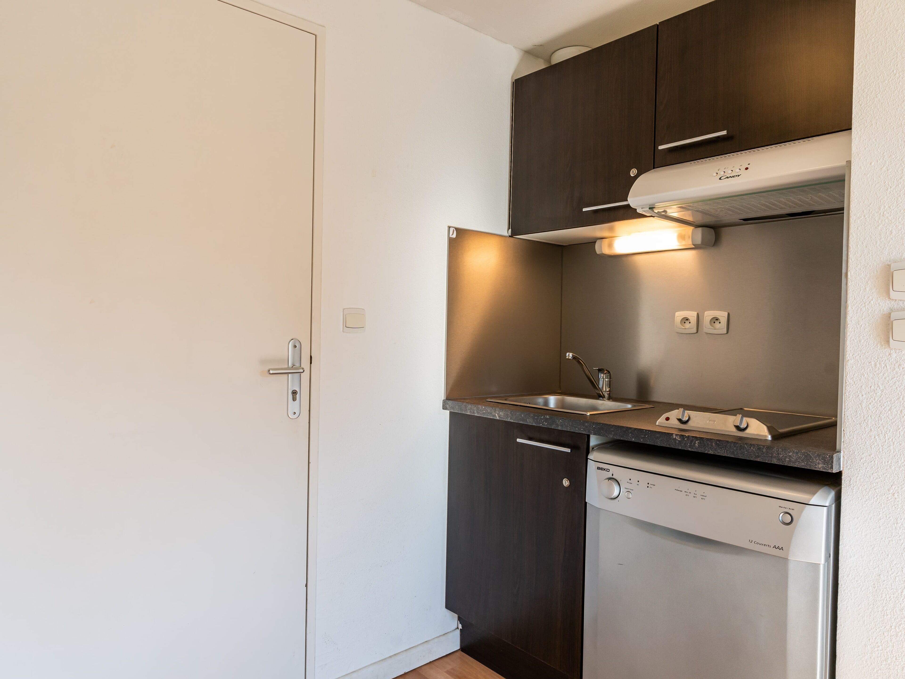 A compact kitchen with a dishwasher, a sink, and dark wooden cabinets.