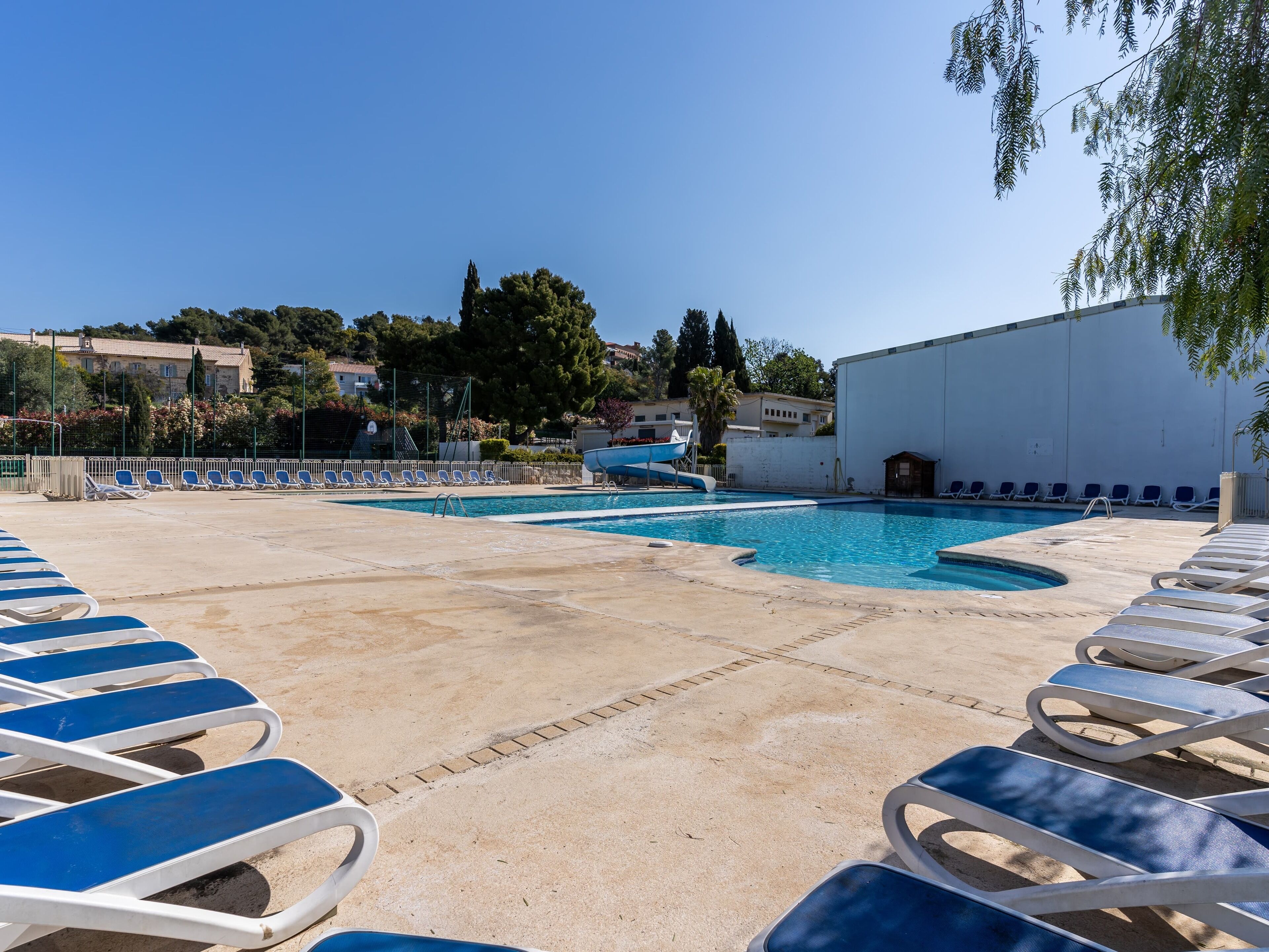 Uma piscina com espreguiçadeiras, um tobogã e um edifício ao fundo.