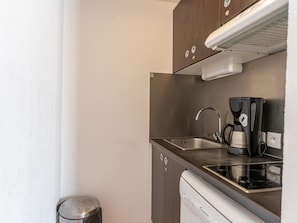 Una kitchenette compacta con un lavamanos de acero inoxidable, una cafetera y un lavavajillas.
