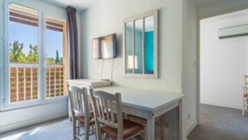 Una habitación con una mesa blanca, dos sillas, un televisor montado en la pared y una ventana con vistas a la vegetación.