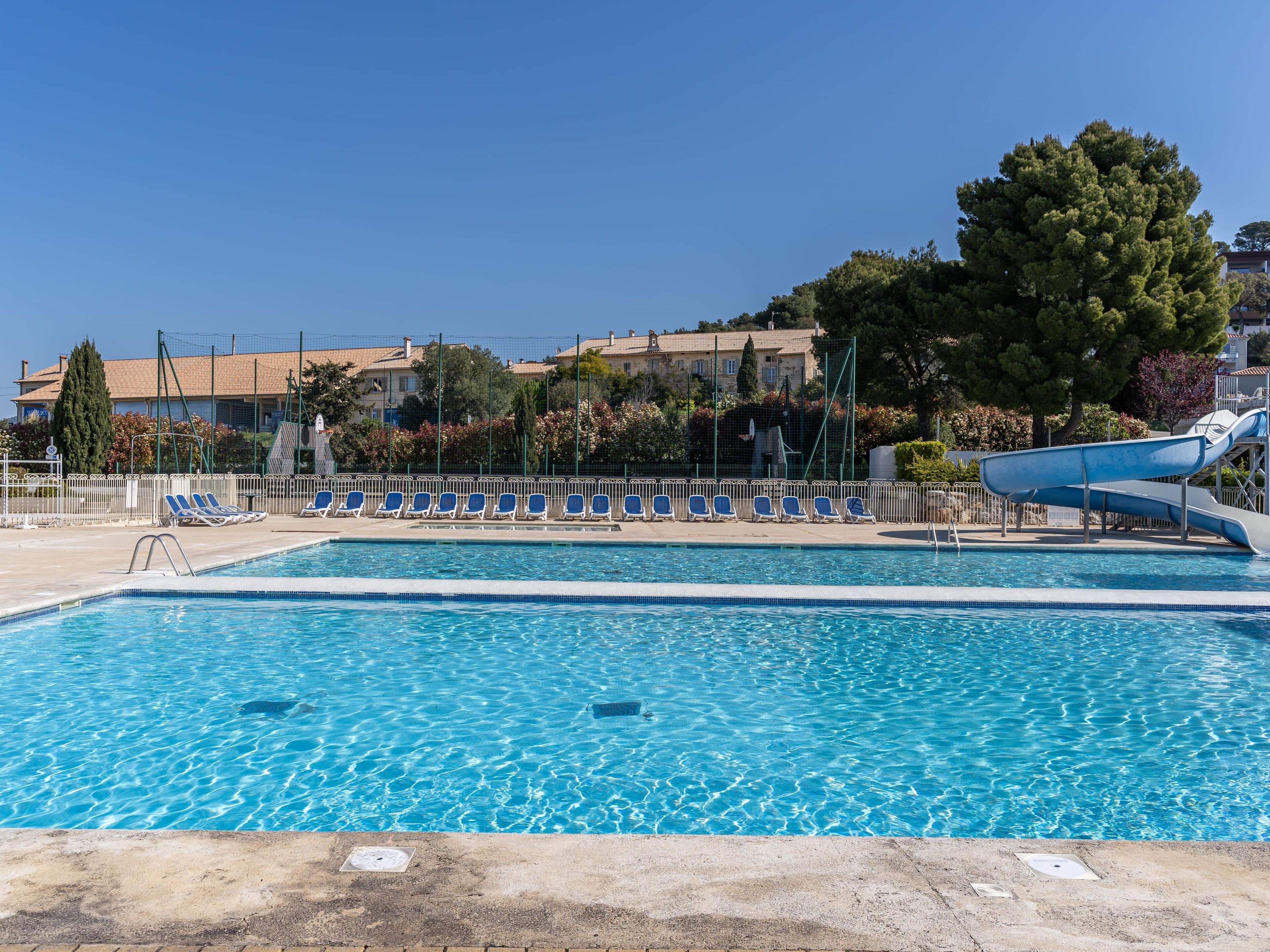 A swimming pool with a water slide, lounge chairs, and a fence.