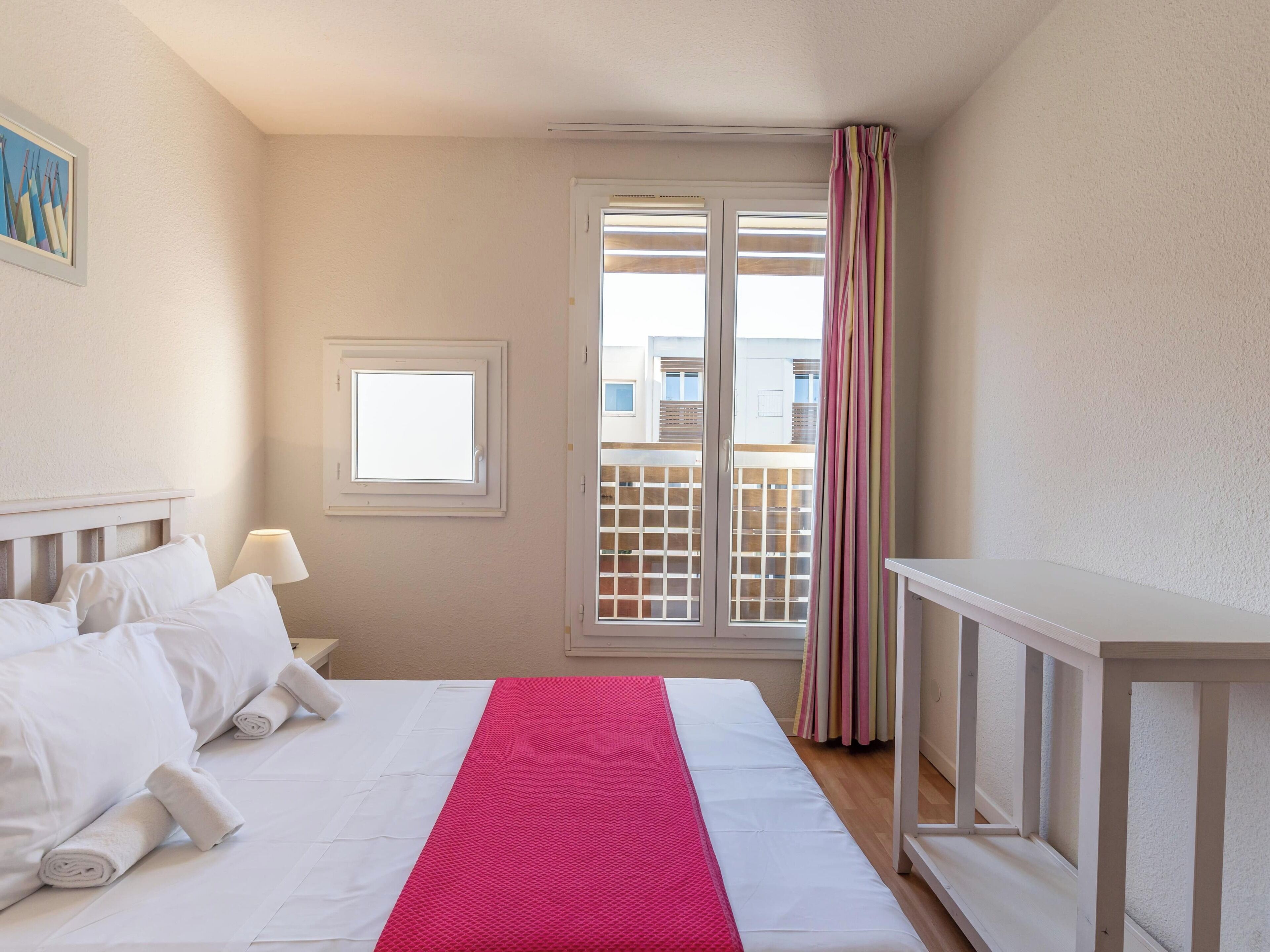 Une chambre d’hôtel avec un lit, une fenêtre, une porte et une vue sur les bâtiments environnants.