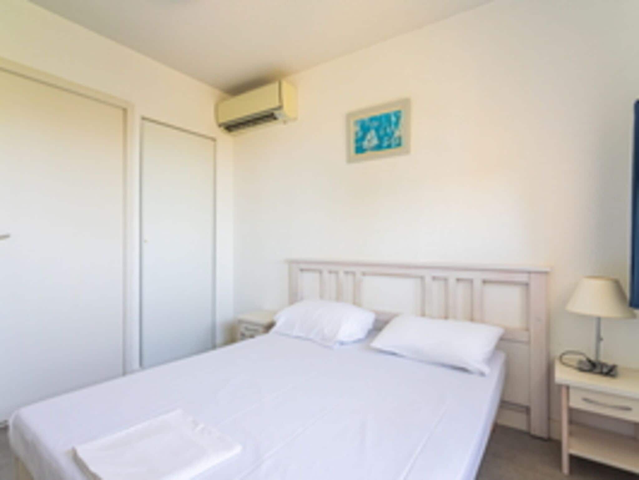 Une chambre à coucher comprenant un lit, une table de chevet, une lampe et un climatiseur fixé au mur.