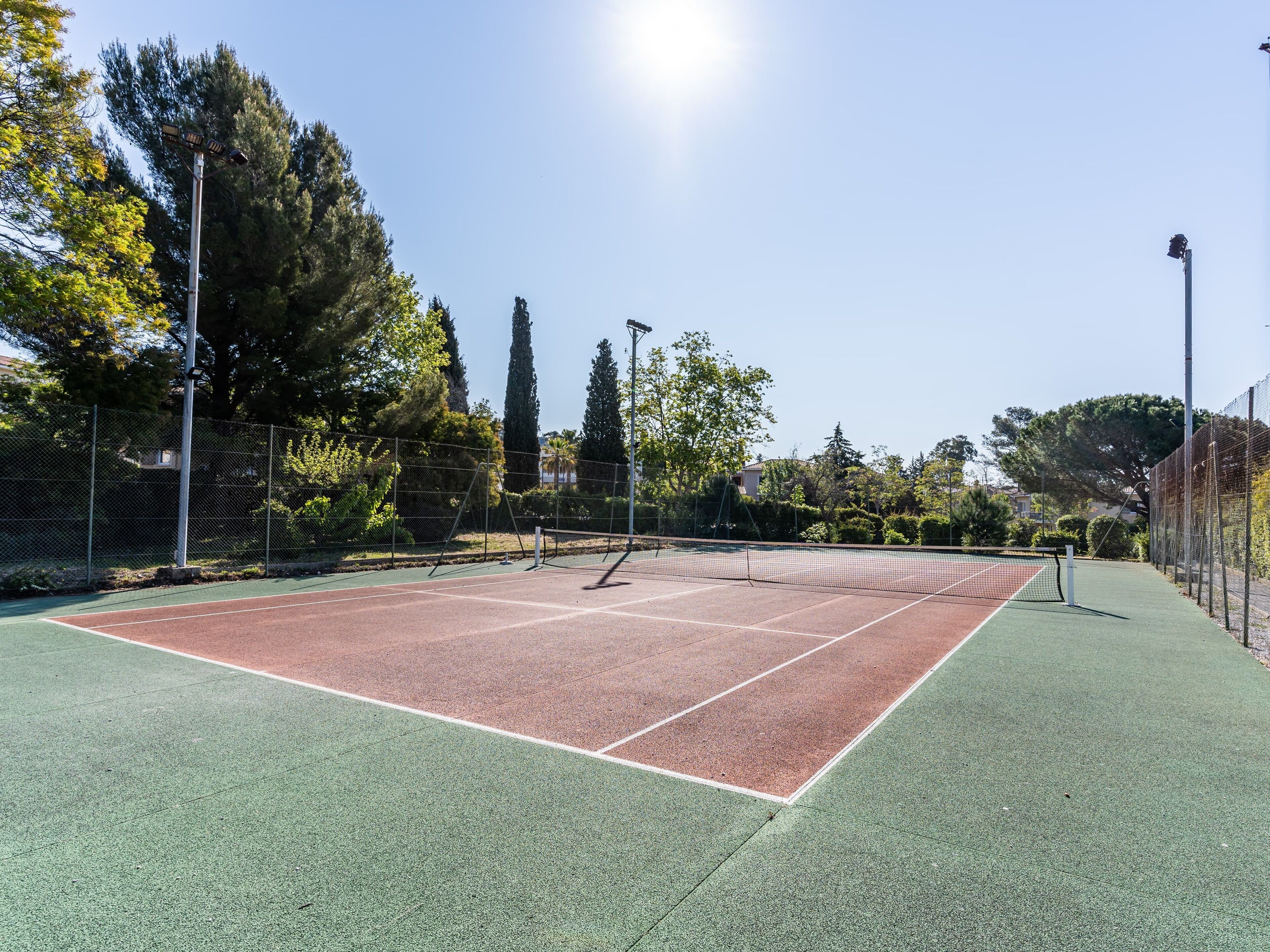 A tennis court with a net, surrounded by trees and a fence.