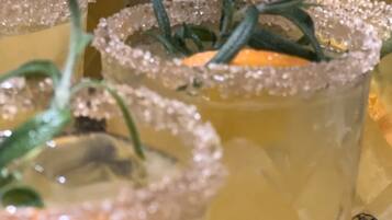 A close-up of several glasses of a yellow beverage garnished with rosemary and sugar.