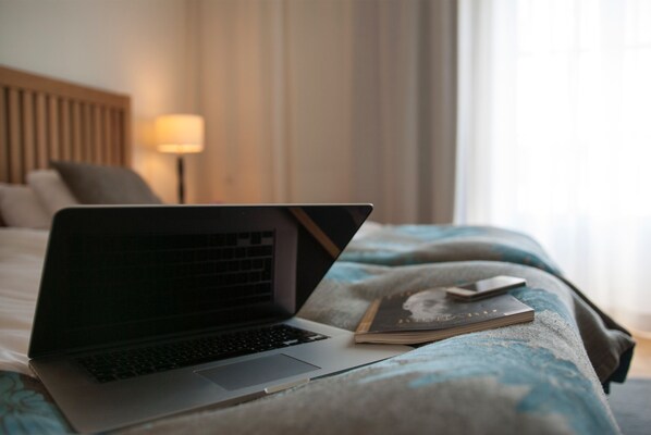 Un ordenador portátil sobre una cama, con un libro y un mando a distancia a su lado.