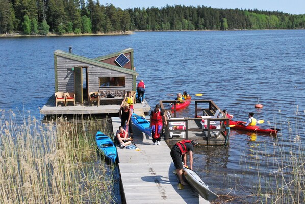 A wooden dock with a small cabin, kayaks, and people engaging in water activities.